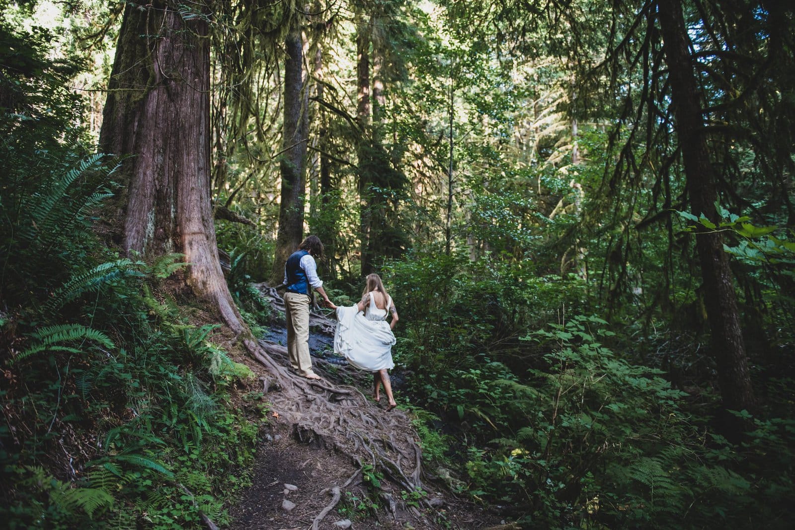 Bride and groom hike in forest.
