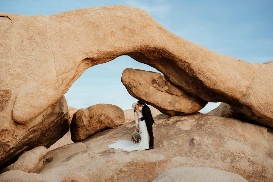 couple kissing beneath arch rock on joshua tree after their elopement