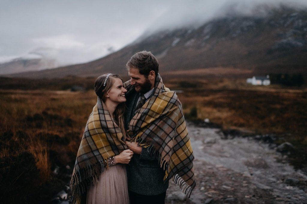 couple snuggling under blanket during their rainy engagement adventure in Glencoe after their handfasting ceremony together.