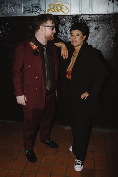 Queer couple both in suits posing for a photo in a Providence club during their elopement. Photo by Rhode Tripper Photography.