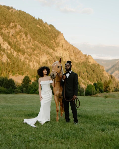 A couple stands in a field with a horse at sunset for their Oregon elopement photos.