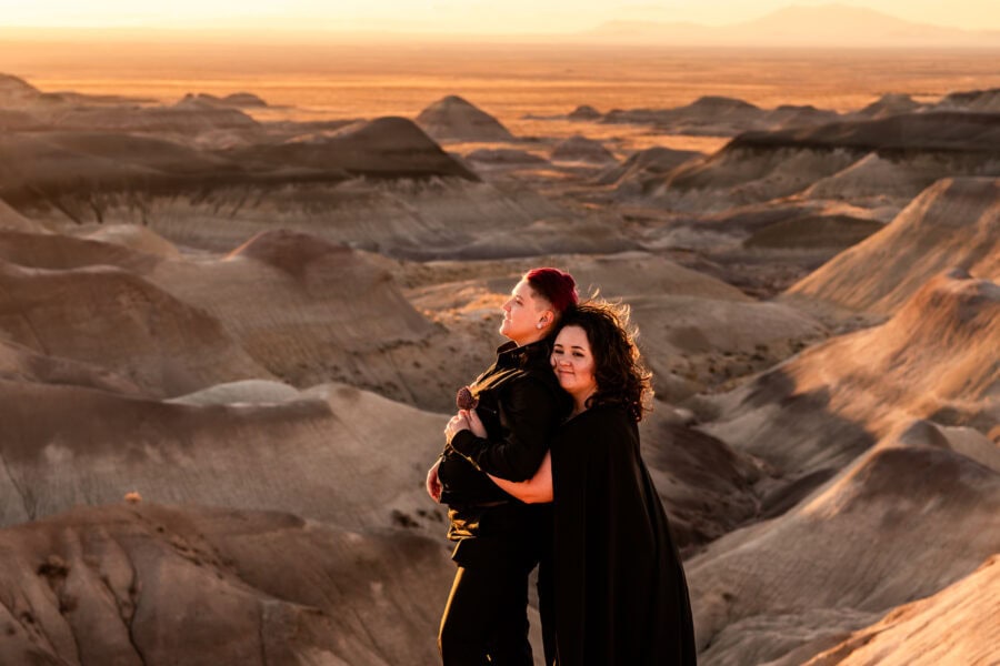 The desert sun sets on this powerful moment, as one partner in a black gown leads the way, cape flowing in the wind.