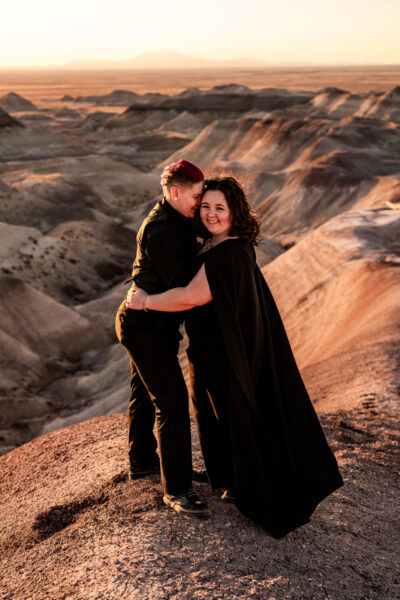 A moment of quiet intimacy between two brides in the Painted Desert, one in a black dress and cape, surrounded by the rich desert terrain.
