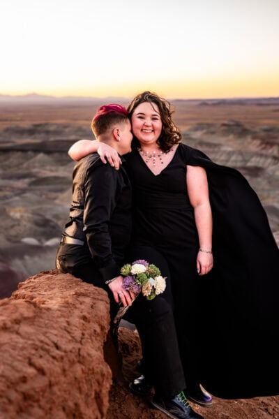 A dreamlike moment in the Painted Desert as the bride in a black dress and cape embraces her partner beneath the Arizona sky.