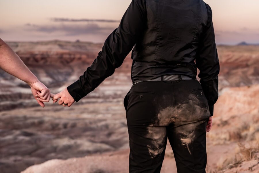 A peaceful moment of reflection in the desert, with one partner in a black wedding dress and cape gazing into the distance.