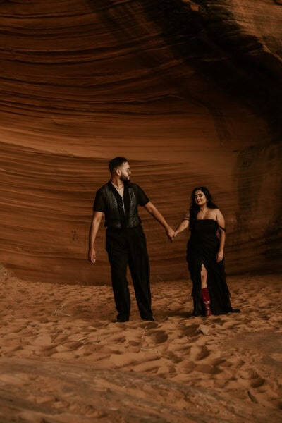 With the desert stretching out before them, the couple walks hand-in-hand through the sandy terrain, their black wedding attire a stunning contrast to the fiery red rocks