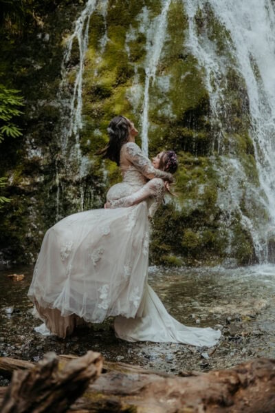 lgbtq wedding couple embrace under a waterfall in olympic national park