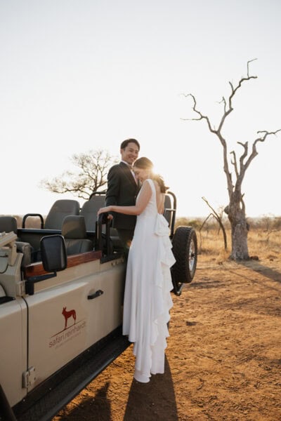 Bride and groom on side of game drive vehicle during the safari elopement in Hoedspruit South Africa.