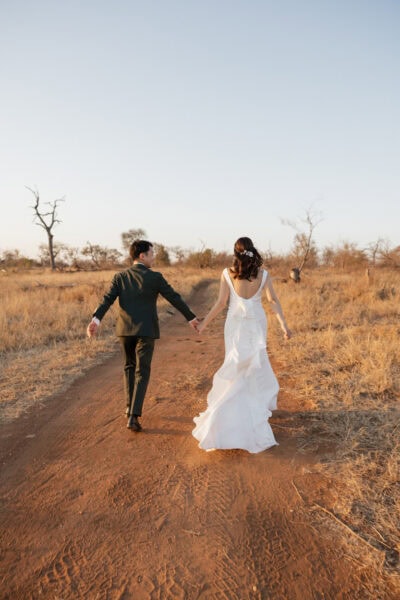 Bride and groom run hand in hand down dirt road during golden hour while enjoying their safari elopement in South Africa.