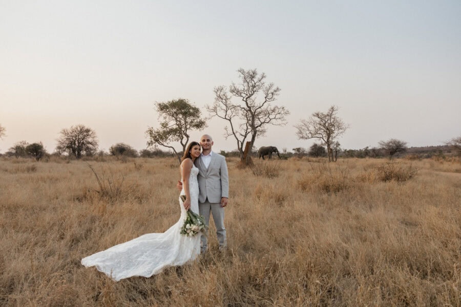 Bride and groom pose for a couples photo during the safari elopement with elephant in the background.