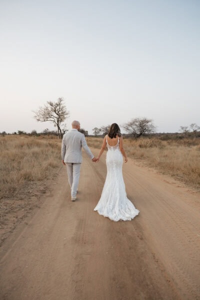 Bride and groom walk down dirt road hand in hand during safari elopement couples portraits