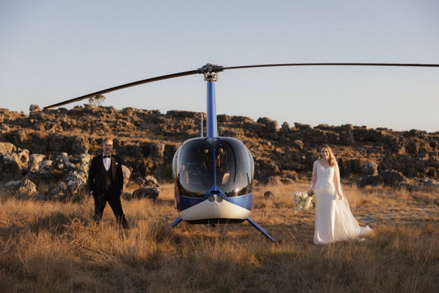 Cinematic helicopter elopement in the Blyde Canyon — couple Standing either side of a blue helicopter on the escarpment with sweeping views across the Lowveld.