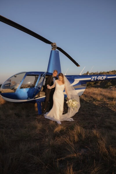 Bride and groom stepping out of a blue helicopter during their Blyde Canyon elopement in Hoedspruit, South Africa, captured at golden hour.